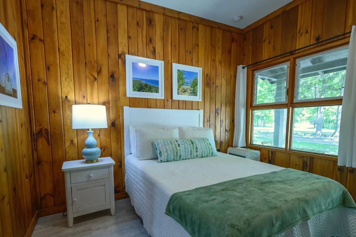 A wooden-paneled bedroom with a bed, nightstand, and window.