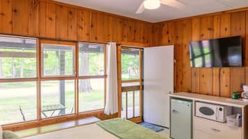A room with wooden walls, a bed, a ceiling fan, a TV, a refrigerator, and a microwave.