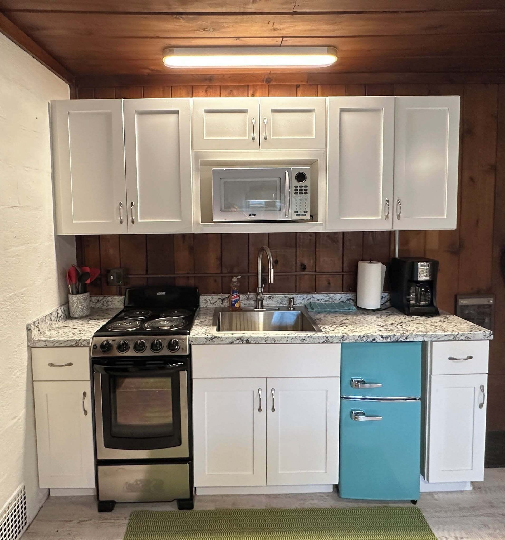 A compact kitchen with white cabinets, a black stove, a microwave, and a blue cabinet.