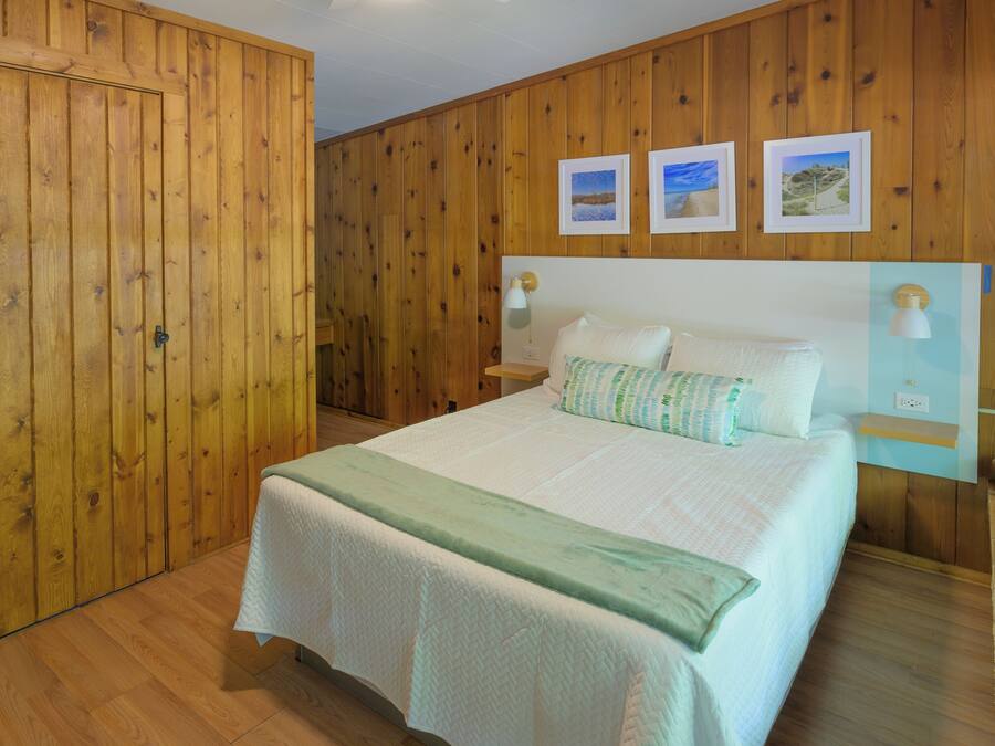 A bedroom with a bed, wooden walls, a ceiling fan, and framed pictures on the wall.