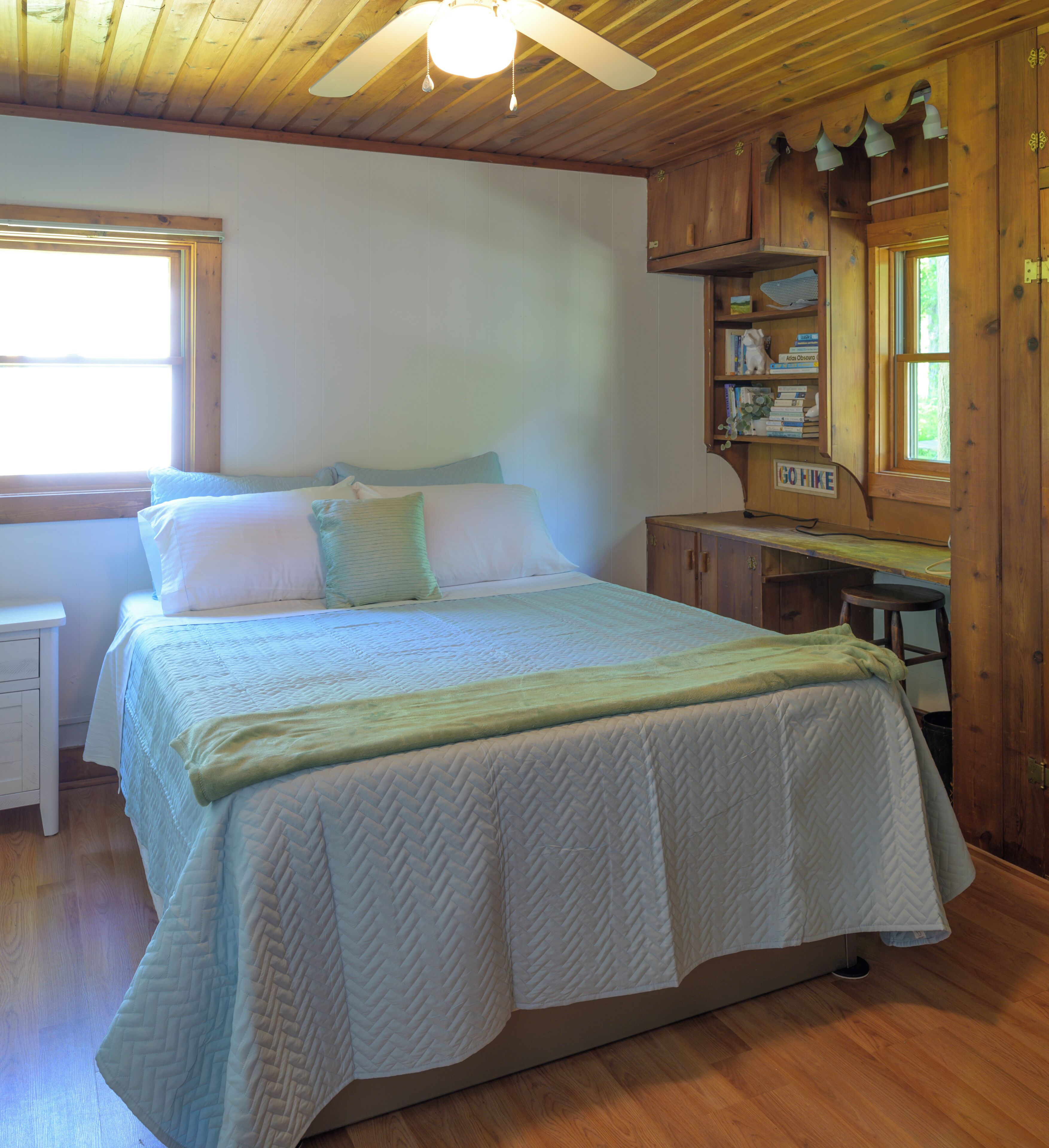 A bedroom with a bed, a nightstand, a wooden headboard, a window, and a bookshelf.