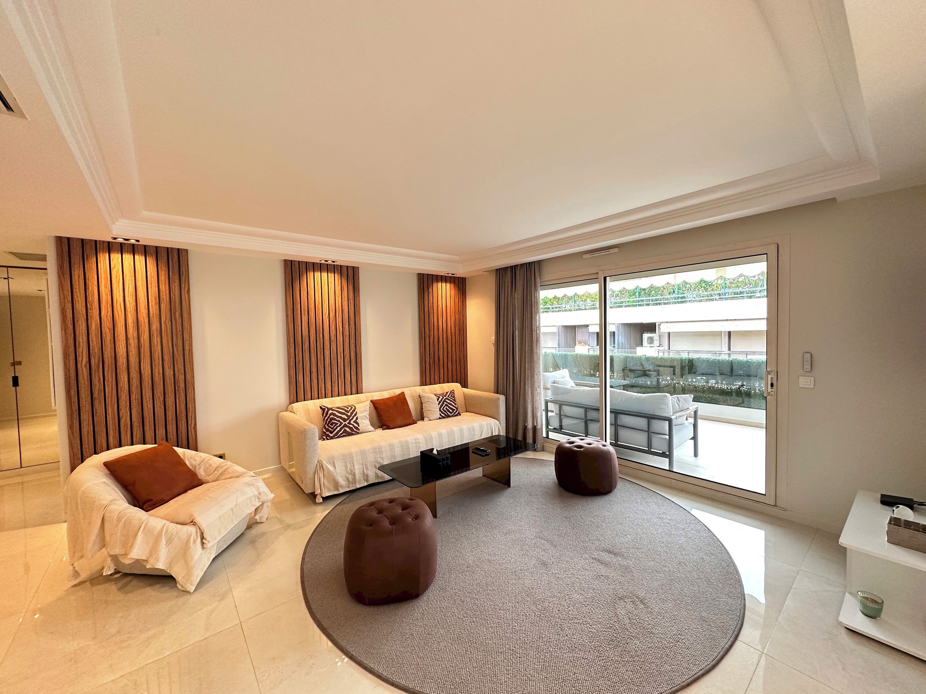 Ein modernes Wohnzimmer mit einer Couch, einem Hocker und einem großen Fenster mit Blick auf einen Pool und Sitzgelegenheiten im Freien.