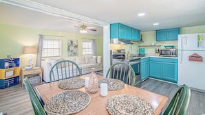 A dining area with a wooden table and chairs, a kitchen with teal cabinets, and a ceiling fan. - 1654 Ocean Lakes Pet Friendly Golf Cart⛱️🏝️🩱🌊👙☀️🐚 (Myrtle Beach)