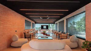 A modern lounge area with a brick wall, comfortable seating, a TV, and large windows. - NOR HOTEL & SPA (Sao Roque)