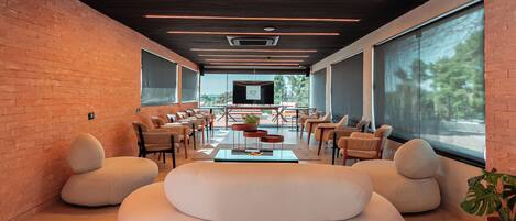 A modern lounge area with a brick wall, comfortable seating, a TV, and large windows.