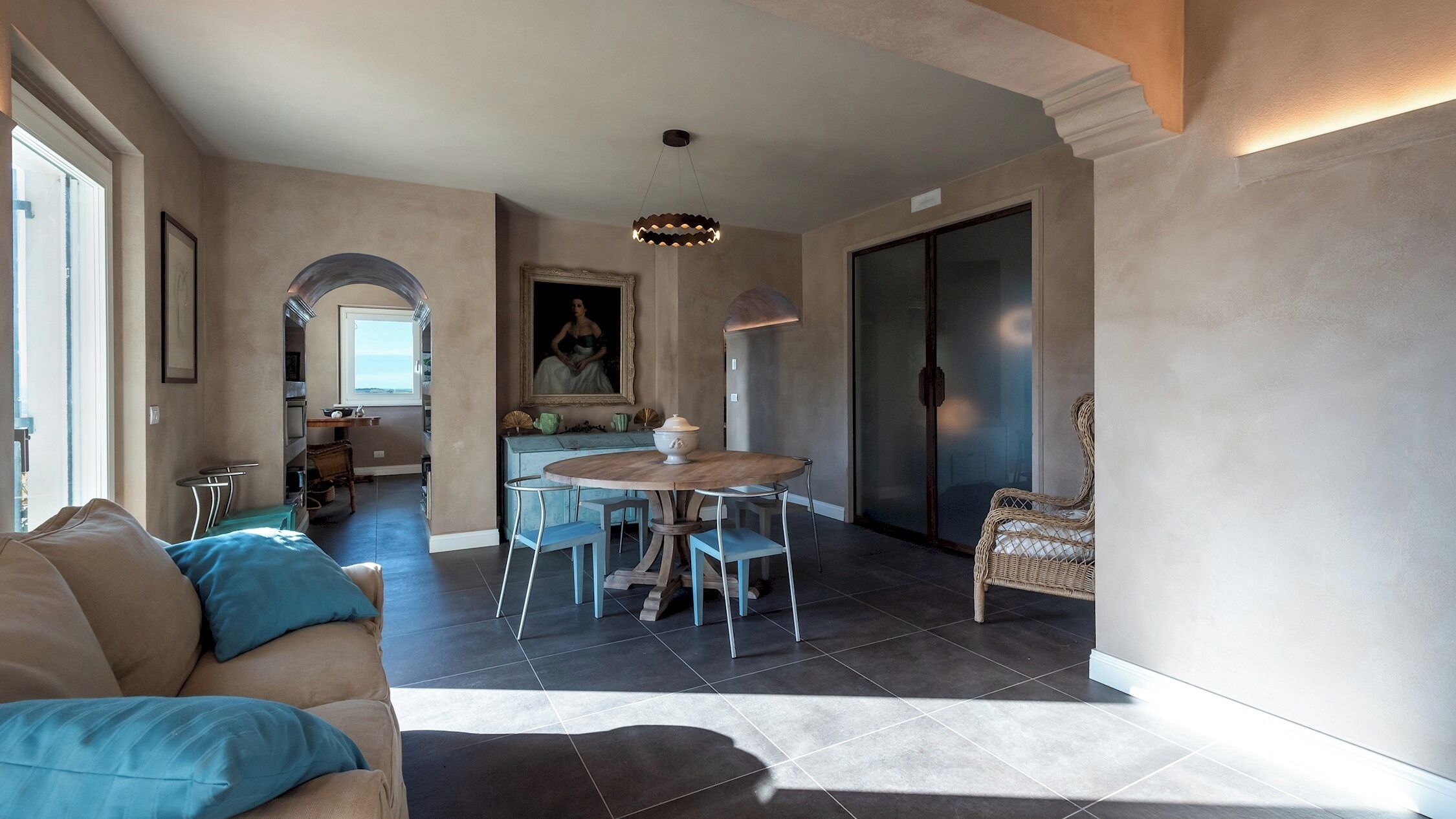 A spacious living area with a round dining table, a sofa with blue cushions, and a wicker chair.
