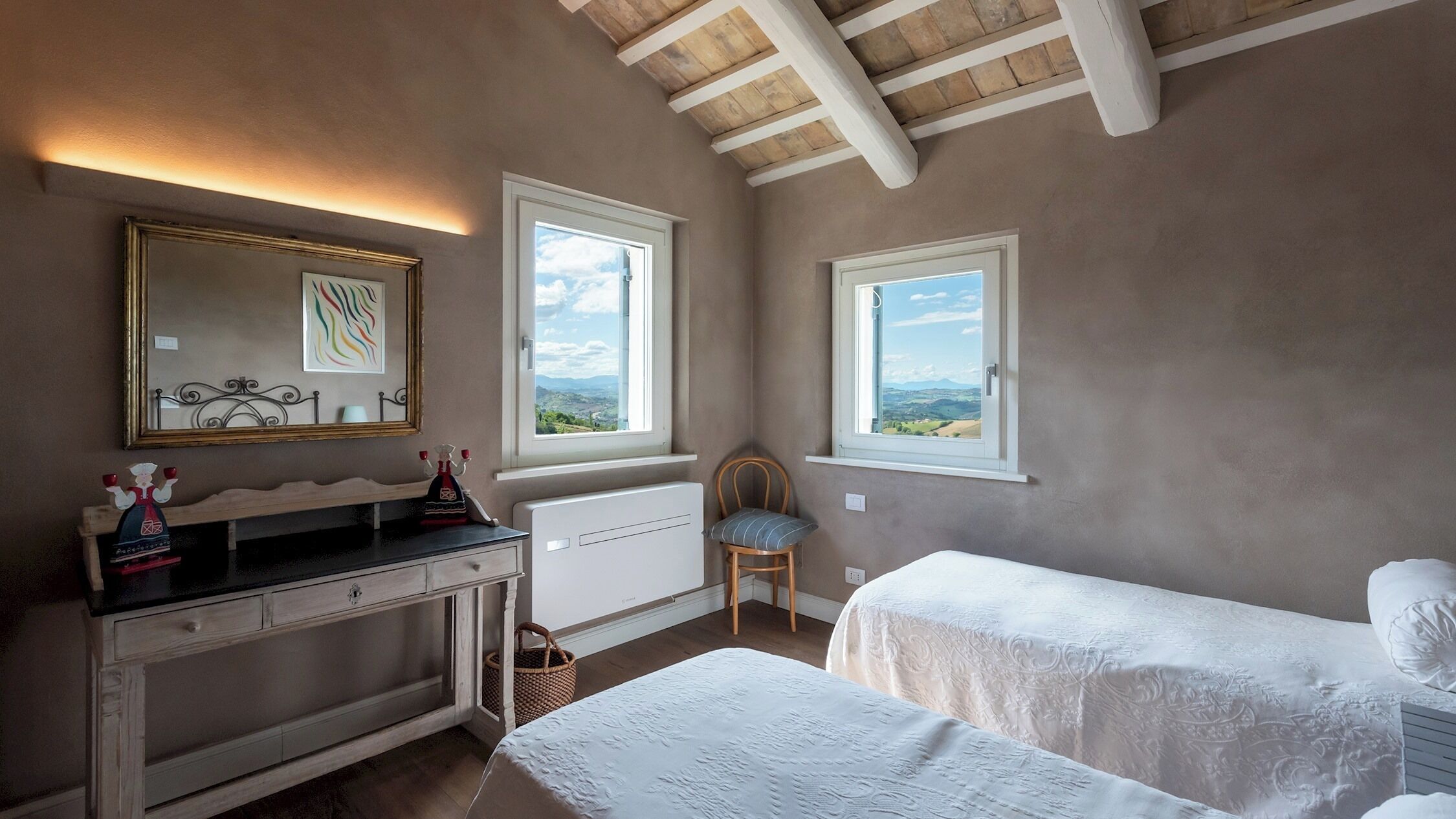 Une chambre avec deux lits simples, une commode, une chaise et deux fenêtres donnant sur la campagne.