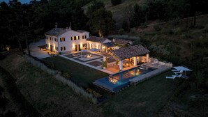 A large, modern house with a swimming pool, multiple outdoor seating areas, and a well-maintained garden.