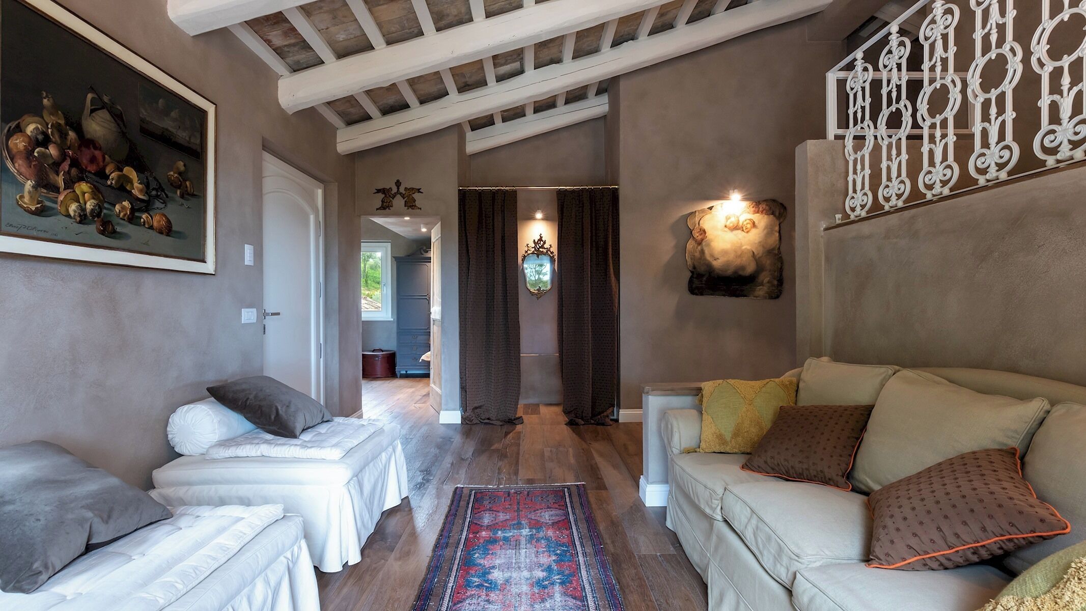 Een woonkamer met een bank, stoelen, een vloerkleed en een schilderij aan de muur.
