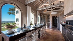 A long dining table set for a meal with a view of a house and landscape.