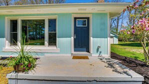 Une maison de plain-pied avec une porte d’entrée, deux fenêtres sur le côté gauche et un petit porche.