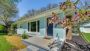 Une maison de plain-pied avec un porche à l’avant, une porte bleue et un petit jardin devant, agrémenté d’un arbre et d’un parterre de fleurs.
