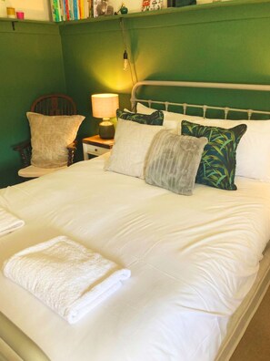 A neatly made bed with white linens and a rolled towel, a bedside lamp, and a chair with cushions. - Chichester House I Secure Garden I Parking I Close to Goodwood (Chichester)