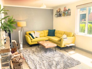 A living room with a yellow sofa, a wooden coffee table, a grey shaggy rug, a floor lamp, and a window with a view of greenery. - Chichester House I Secure Garden I Parking I Close to Goodwood (Chichester)