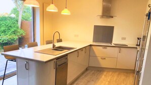 A compact kitchen with a sink, dishwasher, and a stove. There is a window with a view of greenery outside. - Chichester House I Secure Garden I Parking I Close to Goodwood (Chichester)