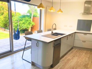 A modern kitchen with a central island, a built-in dishwasher, and a dining area with chairs. - Chichester House I Secure Garden I Parking I Close to Goodwood (Chichester)