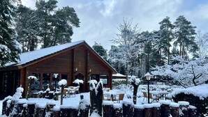Una cabaña de madera con techo nevado, rodeada de árboles cubiertos de nieve y una valla de madera.