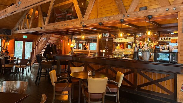 Un interior rústico con vigas de madera, una zona de bar y diferentes distribuciones de asientos.