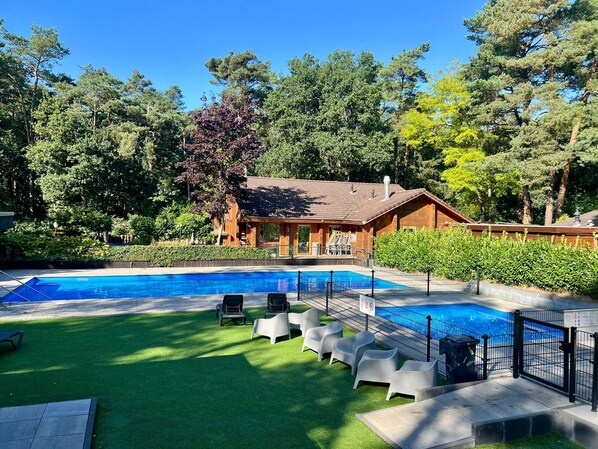 A swimming pool with a wooden building in the background, surrounded by trees.