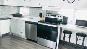A modern kitchen with stainless steel appliances, white cabinetry, and a grey backsplash.