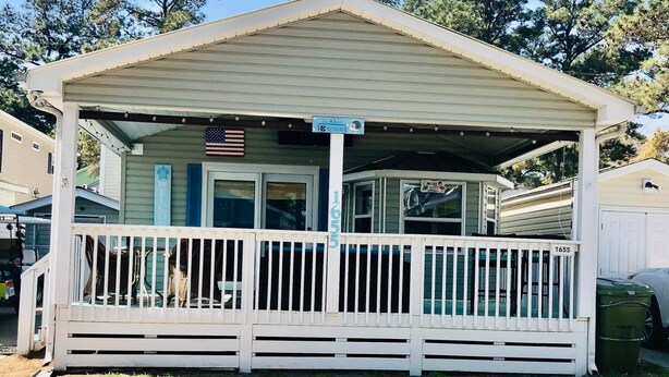 A small, single-story mobile home with a porch and a small deck.
