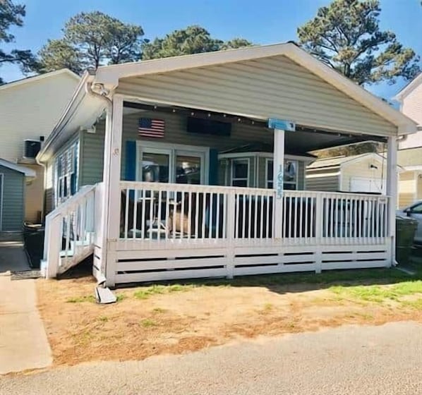 A single-story house with a covered porch, a visible American flag, and a small front yard.