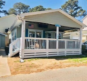 A single-story house with a covered porch, a visible American flag, and a small front yard.