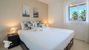 A neatly made bed with white linens and a towel, a nightstand with a lamp, and two wall art pieces depicting nature scenes.