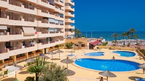 A hotel with multiple balconies, a pool area with two pools, and a view of the sea.