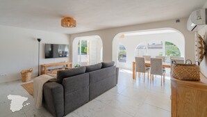Ein modernes Wohnzimmer mit grauem Sofa, einem Flachbildfernseher, einem Holztisch und einem Essbereich mit Stühlen und Tisch.