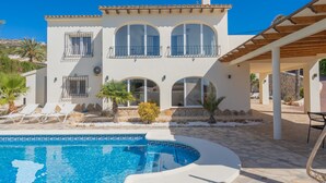 Ein zweistöckiges Haus mit Swimmingpool, einer überdachten Terrasse und Blick auf die umliegende Landschaft.