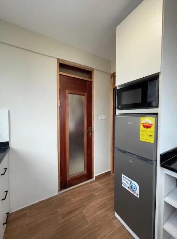 A kitchen with a microwave, refrigerator, and wooden door.