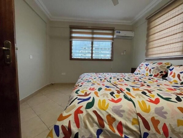 Relax in this cozy space with a comfortable bed, air conditioning, and a window with blinds.