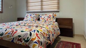 A bedroom with a bed, a window with blinds, an air conditioning unit, and a red rug. - Monie's Quarters (Kumasi)
