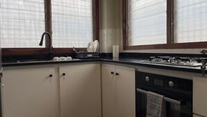 A kitchen with white cabinets, a stove, an oven, and a window with blinds. - Monie's Quarters (Kumasi)