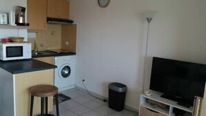 A compact kitchen with a microwave, washing machine, and a small bar stool. A TV is mounted on a stand to the right. - Grand F1 vue mer Dans Résidence Avec Parking et Piscine (Antibes)