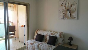 A room with a sofa, a lamp, and a painting on the wall. - Grand F1 vue mer Dans Résidence Avec Parking et Piscine (Antibes)