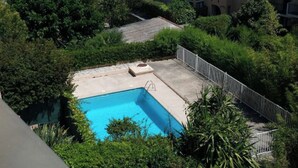 A rectangular swimming pool surrounded by lush greenery, with a concrete deck and a metal fence. - Grand F1 vue mer Dans Résidence Avec Parking et Piscine (Antibes)