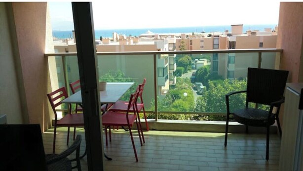 A balcony with a table and chairs, offering a view of a cityscape and greenery. - Grand F1 vue mer Dans Résidence Avec Parking et Piscine (Antibes)