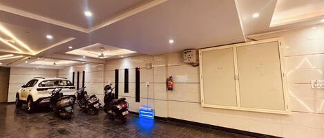 Un estacionamiento con un SUV blanco y varias scooters, un extintor y un panel de control en la pared.