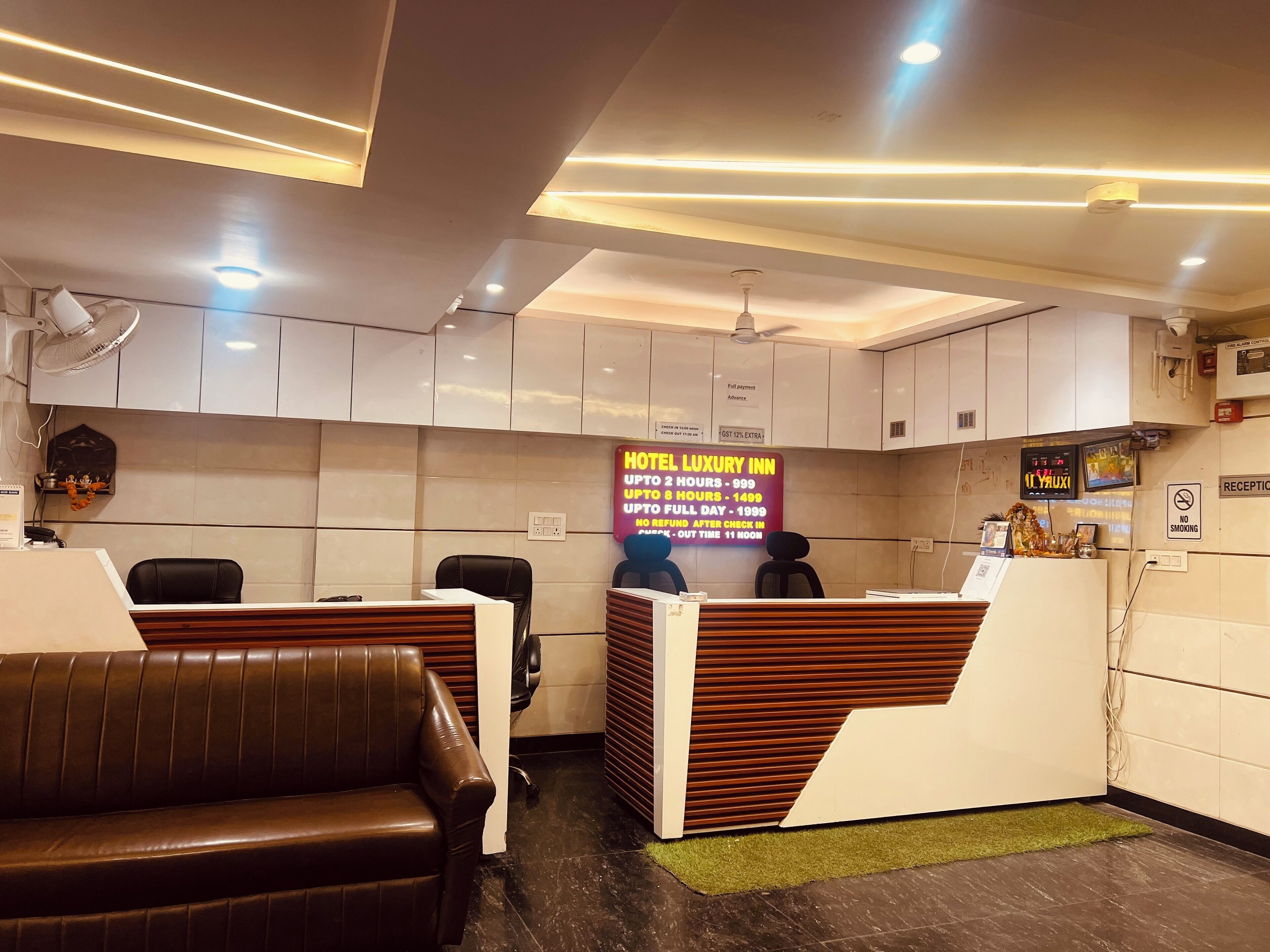 A hotel reception area with a reception desk, leather seating, and a digital display board.