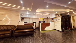 Un espace d’accueil d’hôtel comprenant un comptoir de réception, deux canapés en cuir marron, un écran numérique et un panneau indiquant la réception.