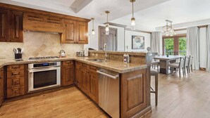 A spacious kitchen with wooden cabinets, a built-in oven, and a dishwasher. There is a dining area with a table and chairs visible through a glass door. - The Aspen Mountain Residences 49AB - 2 Bedroom Residence (Aspen)