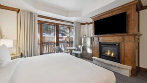Une chambre d’hôtel avec un grand lit, une cheminée, une télévision et un balcon donnant sur l’extérieur.
