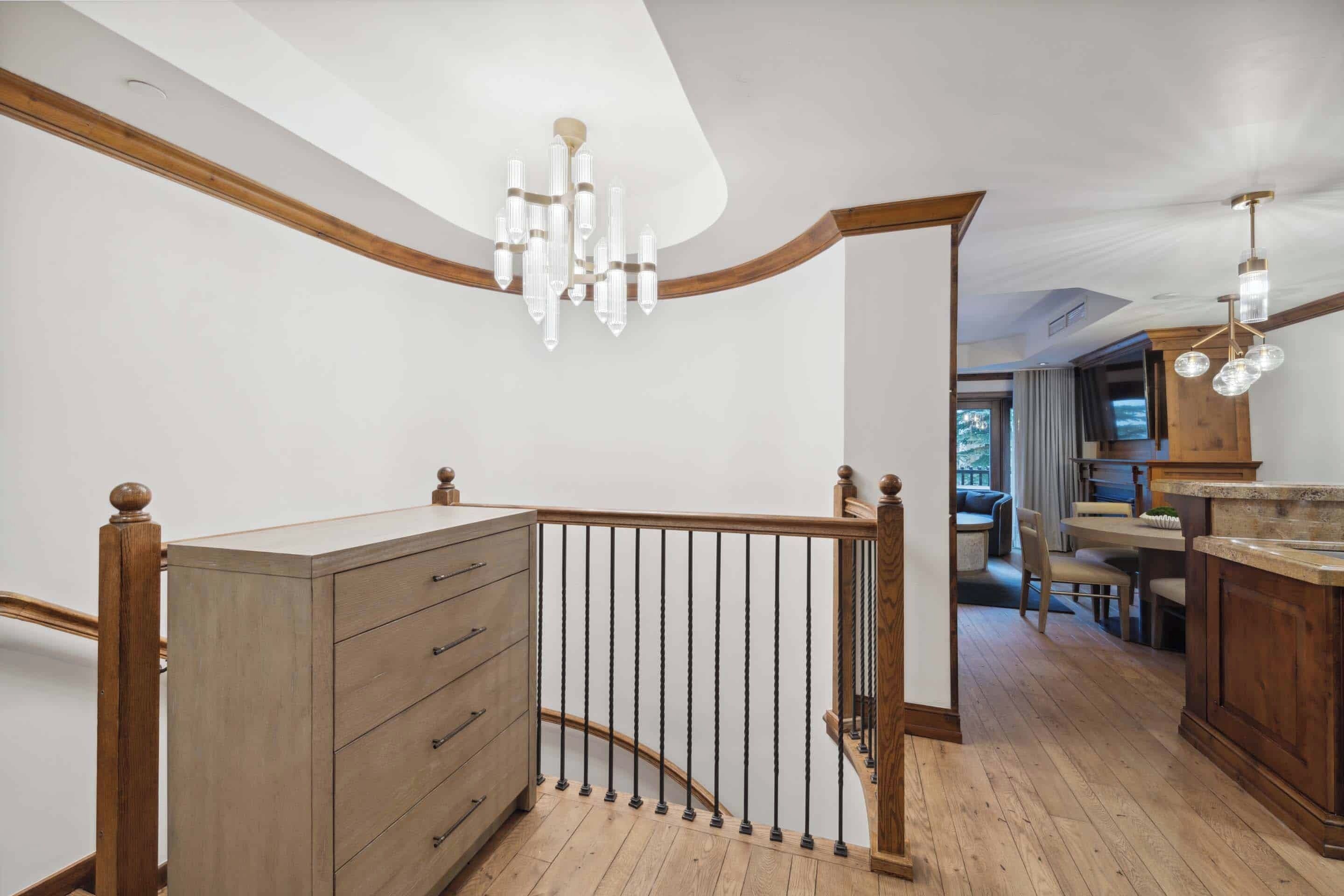 A wooden staircase with a curved railing, a wooden dresser with drawers, and a chandelier.