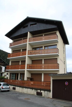 Um edifício com várias andares, varandas, portão fechado e estacionamento.
