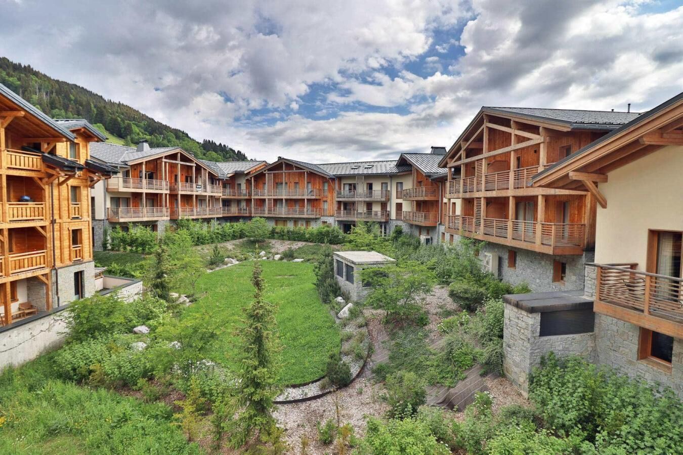 A hotel with multiple wooden balconies, a central courtyard with a grassy area, and stone walls.