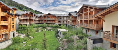 A hotel with multiple wooden balconies, a central courtyard with a grassy area, and stone walls.