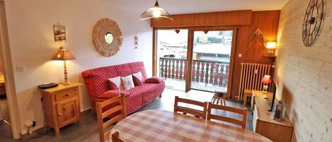 A cozy room with a dining table, chairs, a red sofa, and a balcony with a railing.