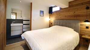 A bedroom with a large bed, wooden panel walls, a built-in wardrobe, and a small window.